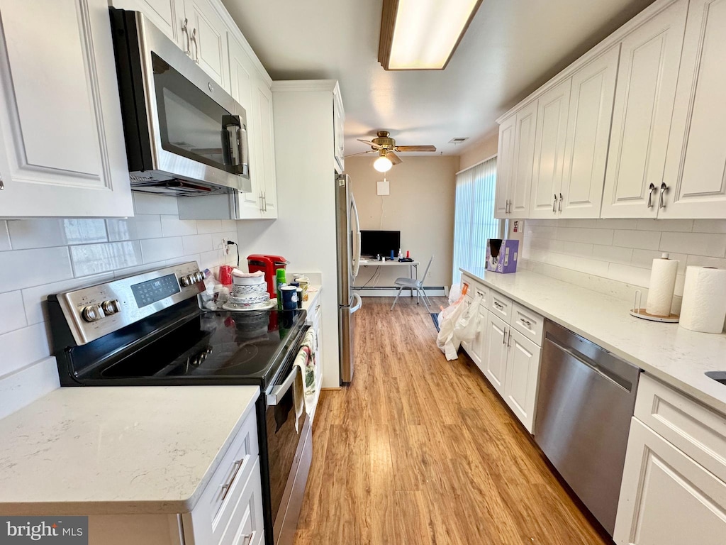 kitchen with light wood finished floors, appliances with stainless steel finishes, white cabinetry, and tasteful backsplash