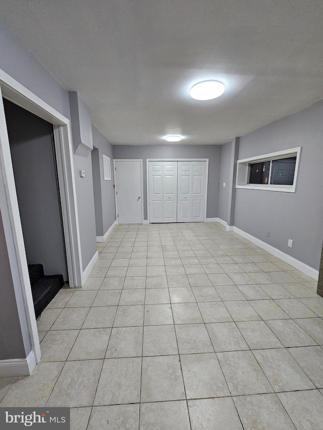 unfurnished room featuring light tile patterned flooring, stairway, and baseboards