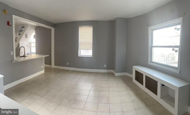 unfurnished living room with light tile patterned floors, stairway, a sink, and baseboards