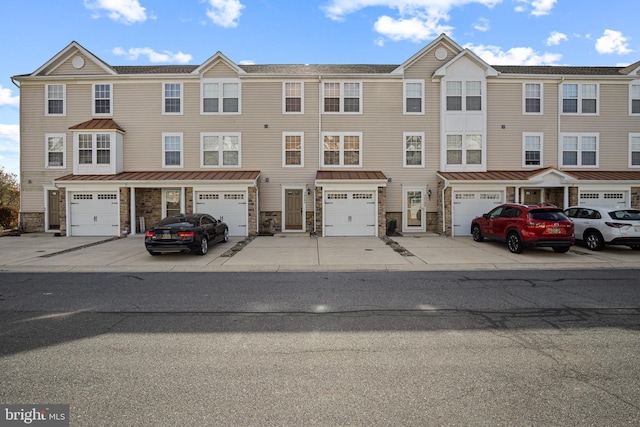 townhome / multi-family property featuring stone siding, driveway, an attached garage, and a standing seam roof