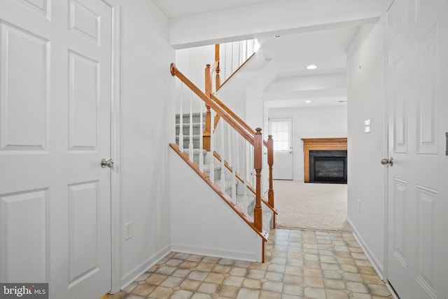 foyer featuring recessed lighting, light colored carpet, baseboards, stairway, and a glass covered fireplace