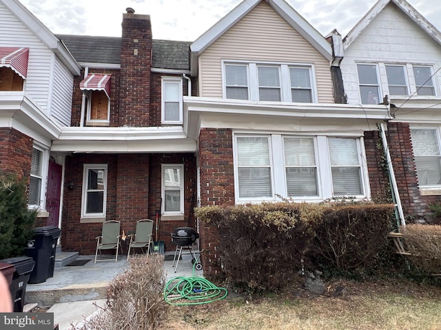 view of front facade with a patio area, brick siding, and a chimney