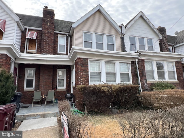 townhome / multi-family property with a chimney, a porch, and brick siding