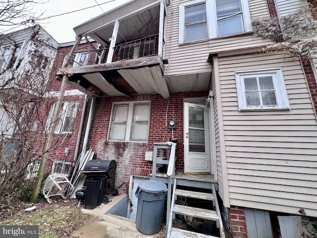 view of exterior entry featuring a balcony and brick siding