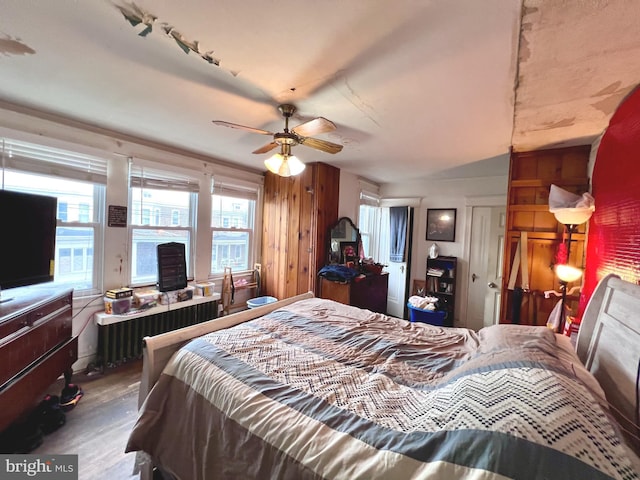 bedroom featuring wood walls, radiator heating unit, and ceiling fan