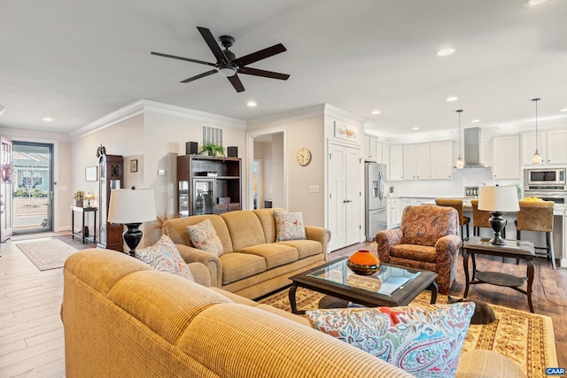 living room with light wood-type flooring, a ceiling fan, crown molding, and recessed lighting