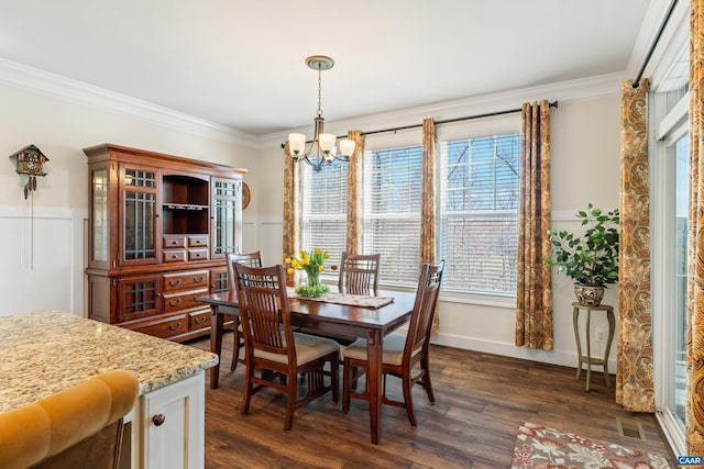 dining area with a decorative wall, a notable chandelier, dark wood-style flooring, ornamental molding, and wainscoting