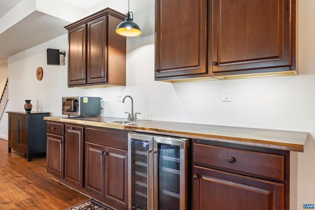 kitchen with pendant lighting, dark wood-style flooring, stainless steel microwave, a sink, and beverage cooler