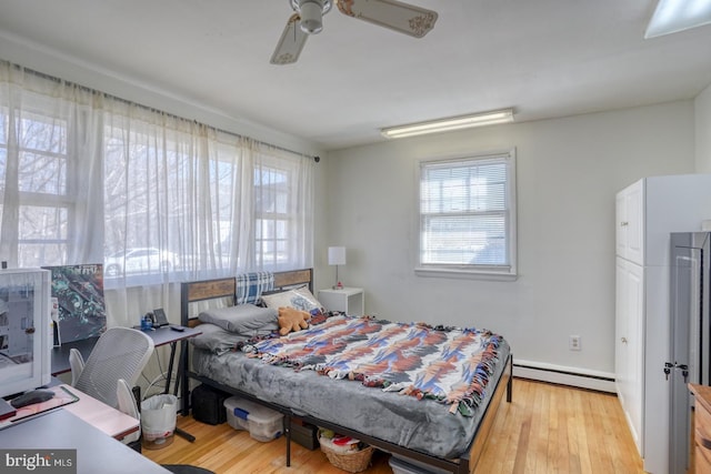 bedroom featuring a ceiling fan, a baseboard heating unit, and wood finished floors