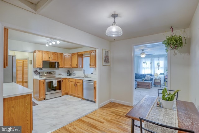 kitchen featuring stainless steel appliances, a sink, light countertops, light wood-type flooring, and pendant lighting