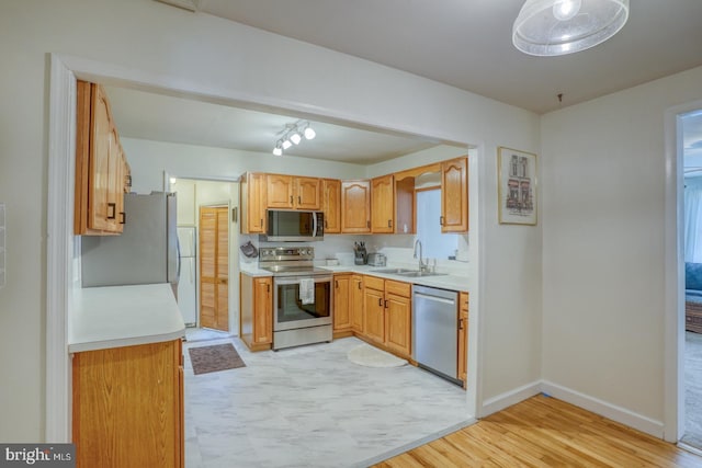 kitchen featuring light wood finished floors, baseboards, stainless steel appliances, light countertops, and a sink