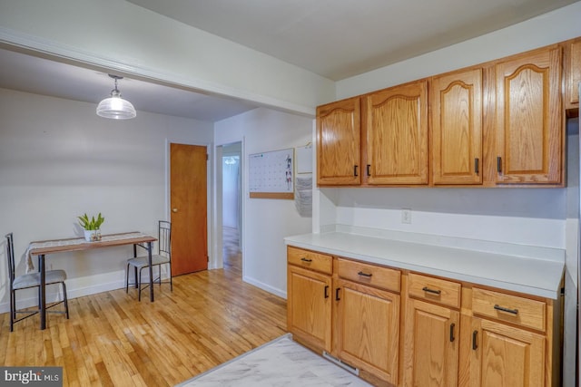 kitchen featuring baseboards, light countertops, hanging light fixtures, brown cabinets, and light wood finished floors