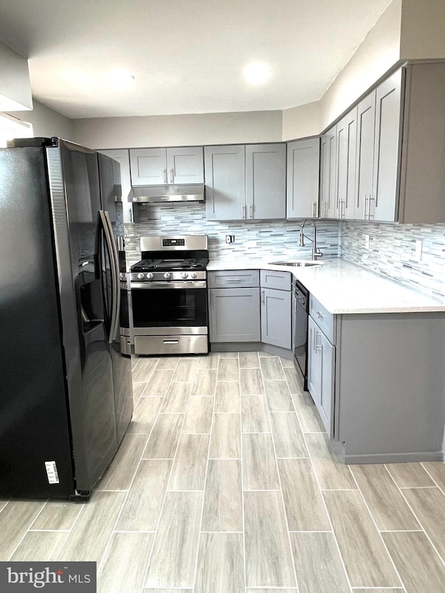 kitchen with gray cabinetry, gas stove, a sink, fridge with ice dispenser, and under cabinet range hood