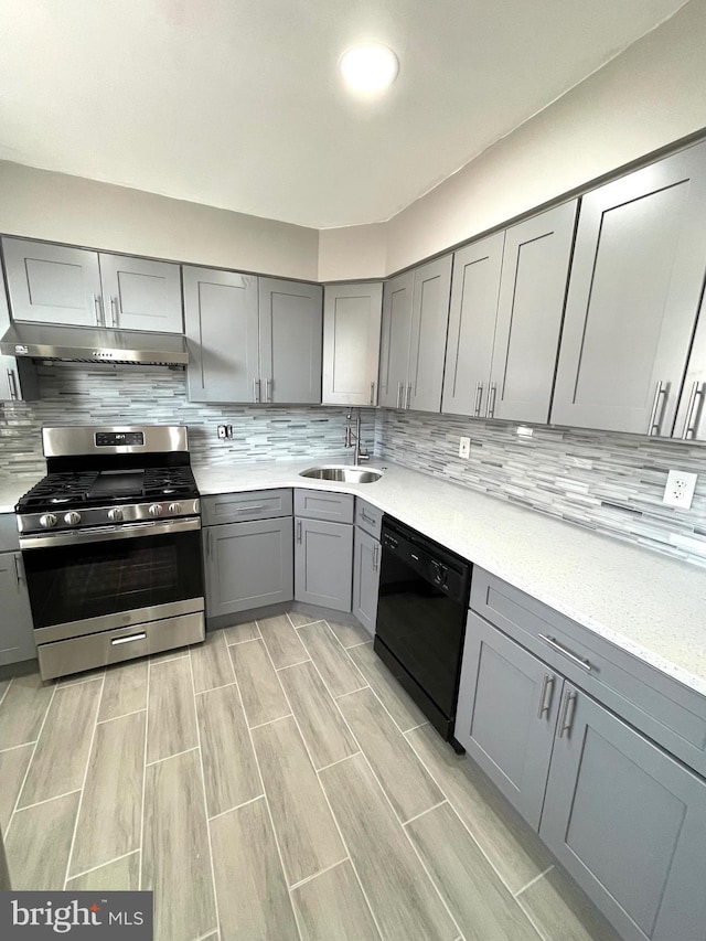 kitchen featuring stainless steel gas range oven, under cabinet range hood, gray cabinetry, a sink, and dishwasher