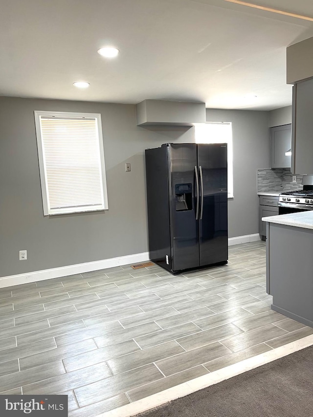 kitchen featuring wood tiled floor, light countertops, black refrigerator with ice dispenser, gray cabinetry, and stainless steel range with gas stovetop