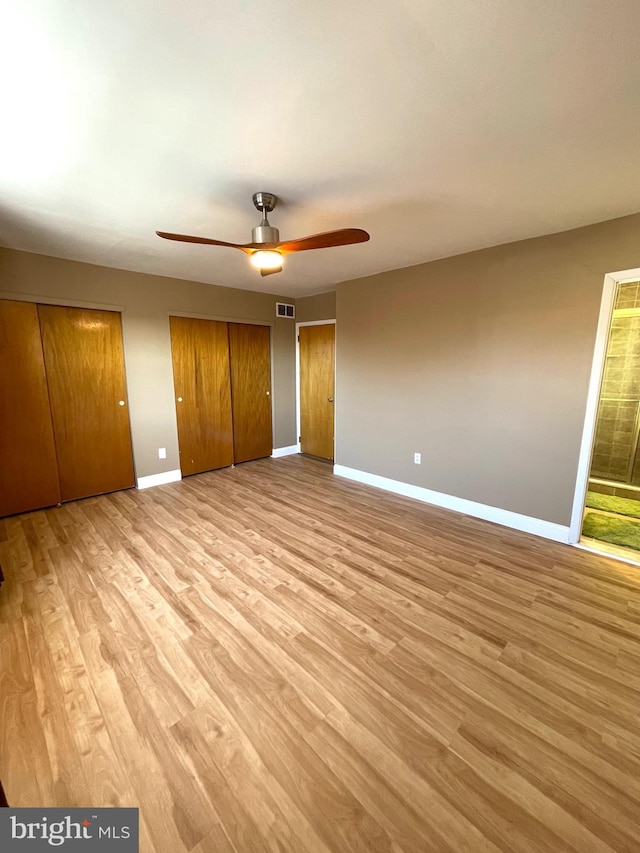 unfurnished bedroom featuring light wood finished floors, multiple closets, visible vents, a ceiling fan, and baseboards