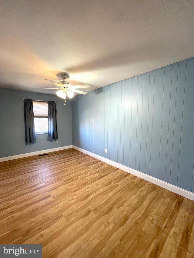 empty room with baseboards, light wood-style flooring, visible vents, and a ceiling fan