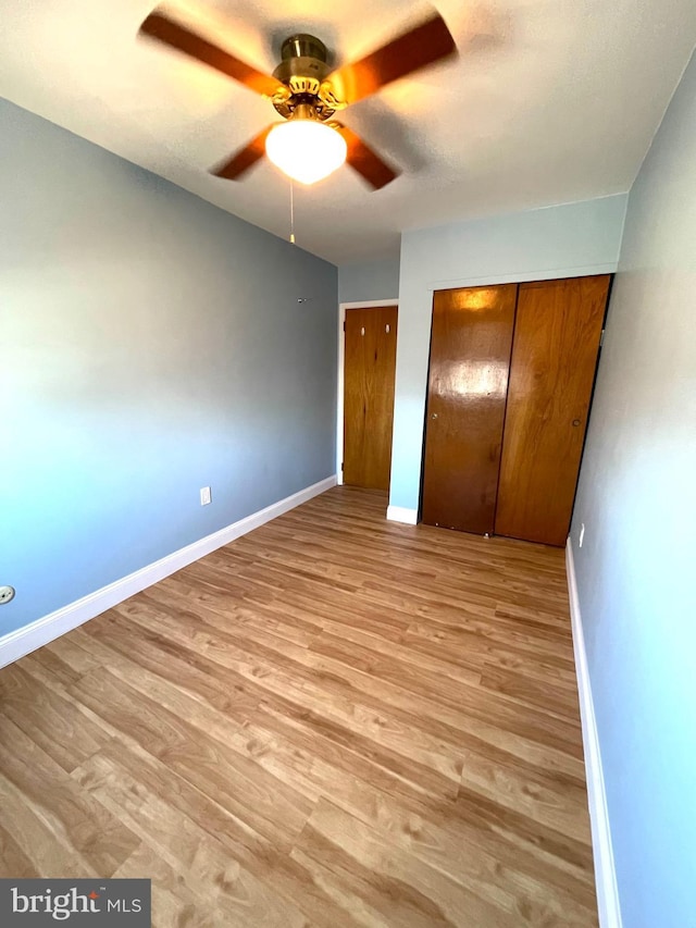 unfurnished bedroom featuring light wood-style floors, a ceiling fan, baseboards, and two closets