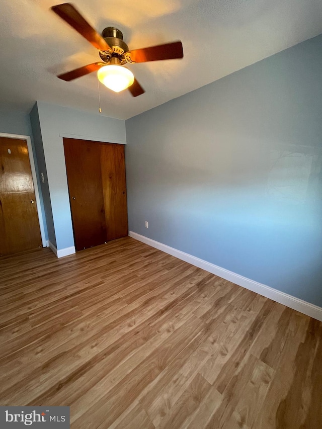 unfurnished bedroom featuring a closet, ceiling fan, baseboards, and wood finished floors