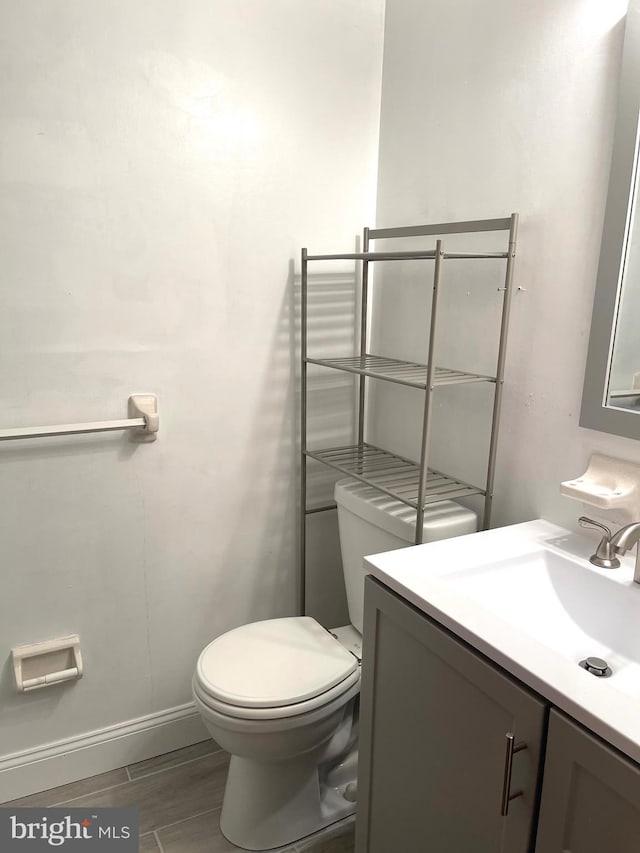 bathroom featuring wood finish floors, baseboards, vanity, and toilet