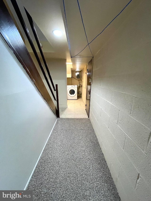 hall featuring light carpet, washer / dryer, and concrete block wall