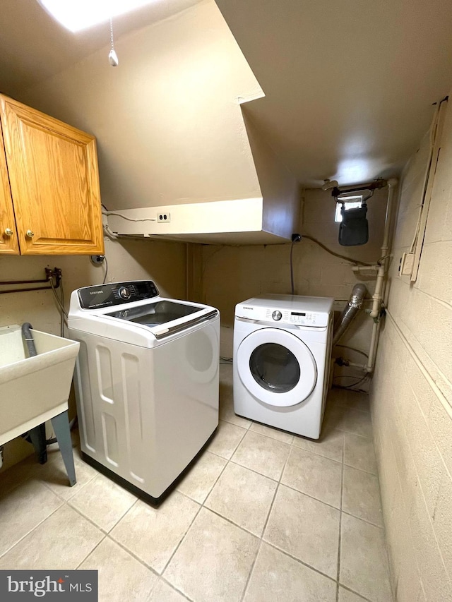 clothes washing area featuring concrete block wall, cabinet space, separate washer and dryer, and light tile patterned flooring