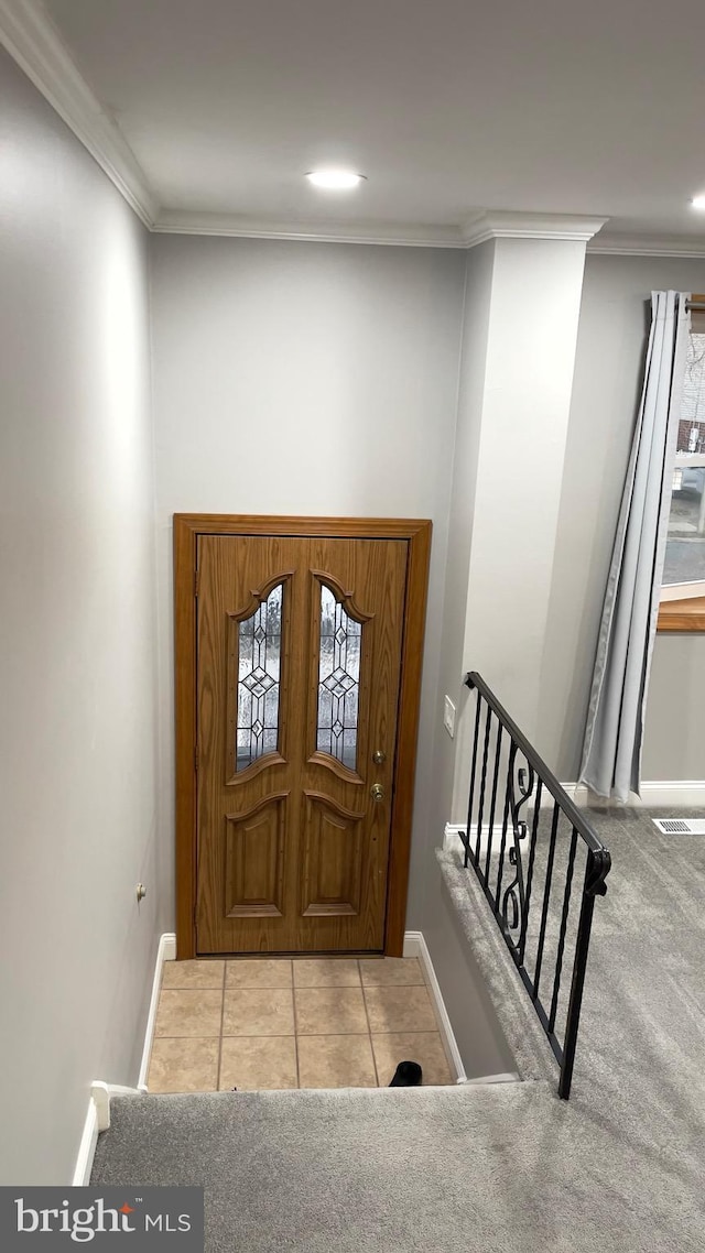 tiled entrance foyer with carpet floors, ornamental molding, and baseboards