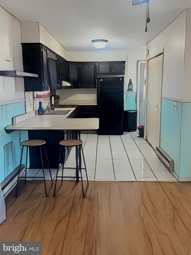 kitchen featuring a kitchen breakfast bar, freestanding refrigerator, a peninsula, light countertops, and dark cabinetry