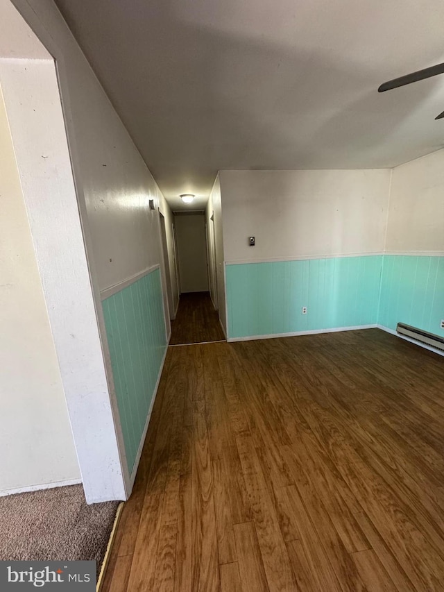 interior space featuring a wainscoted wall, a baseboard radiator, wood finished floors, and a ceiling fan