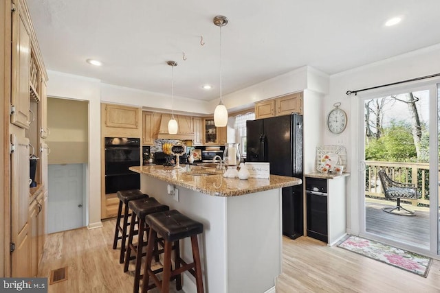 kitchen featuring a breakfast bar, visible vents, light wood-style floors, light brown cabinets, and an island with sink