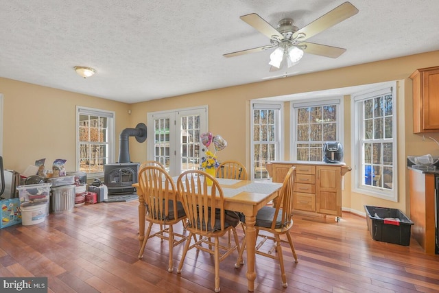 dining room featuring a textured ceiling, a wood stove, light wood-style flooring, and a ceiling fan