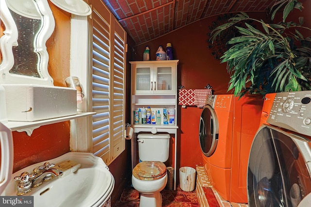 bathroom featuring lofted ceiling, toilet, a sink, brick ceiling, and independent washer and dryer