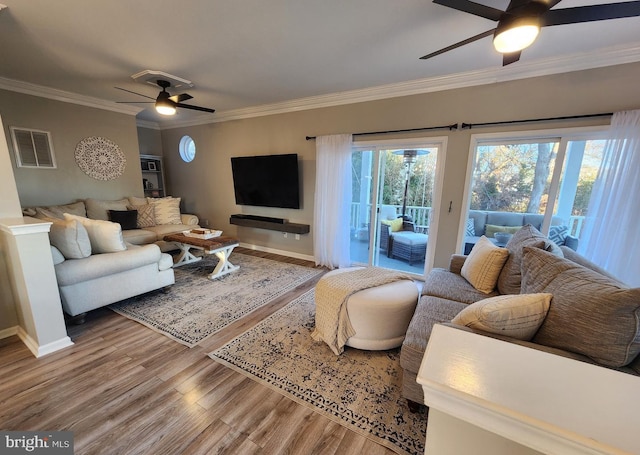 living room featuring wood finished floors, visible vents, baseboards, a ceiling fan, and crown molding