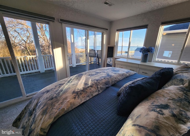 bedroom with access to exterior, visible vents, carpet floors, and a textured ceiling