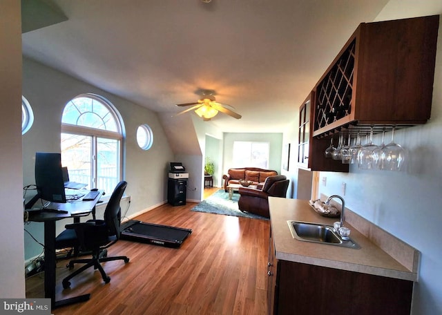 office area featuring ceiling fan, a sink, wood finished floors, bar area, and baseboards