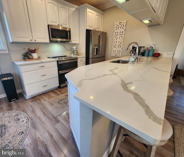 kitchen with light wood-style flooring, a breakfast bar area, appliances with stainless steel finishes, a peninsula, and a sink