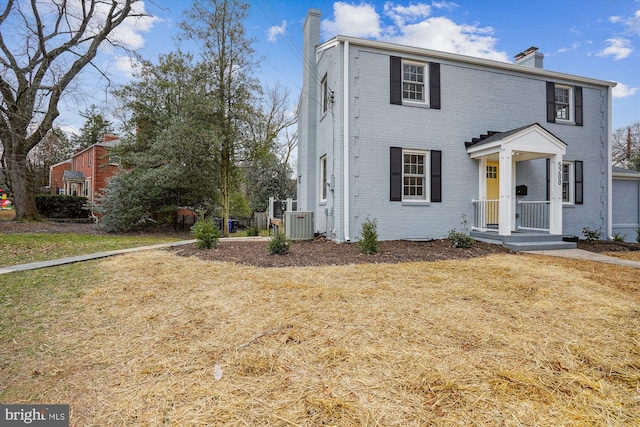 view of front of house with a front yard, brick siding, a chimney, and central air condition unit