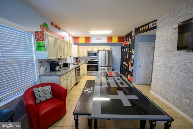 kitchen with light tile patterned floors, stainless steel appliances, visible vents, a sink, and brick wall