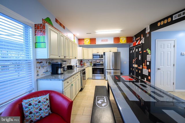 kitchen featuring stainless steel appliances, tasteful backsplash, visible vents, a sink, and light stone countertops