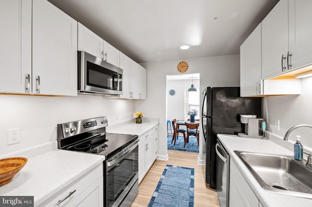 kitchen with appliances with stainless steel finishes, light countertops, light wood-style floors, and a sink