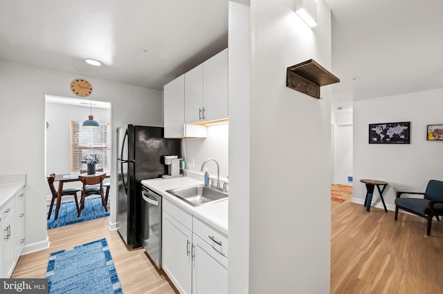 kitchen featuring dishwasher, light countertops, light wood-style floors, white cabinetry, and a sink