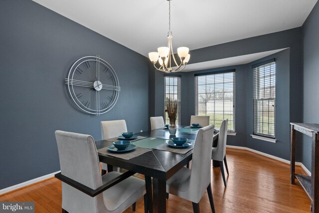 dining room featuring a notable chandelier, baseboards, wood finished floors, and a healthy amount of sunlight