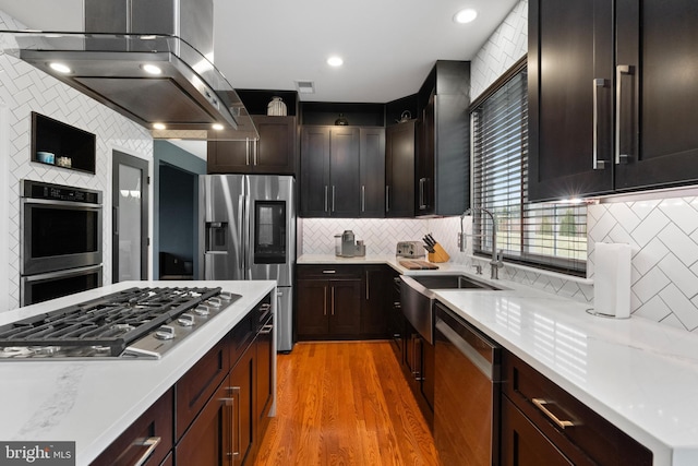kitchen with appliances with stainless steel finishes, a sink, light countertops, extractor fan, and decorative backsplash