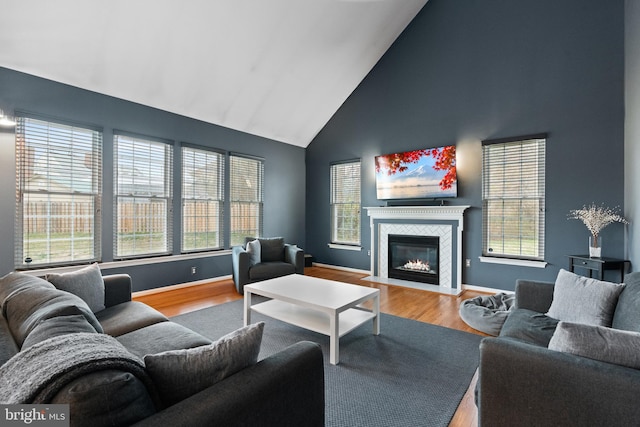 living area featuring high vaulted ceiling, a tiled fireplace, baseboards, and wood finished floors