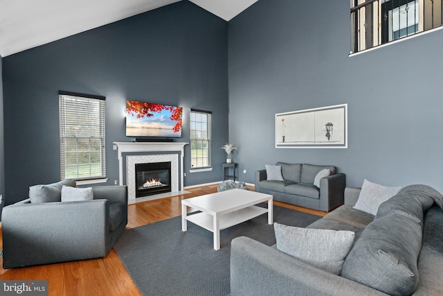 living room featuring a healthy amount of sunlight, a tile fireplace, high vaulted ceiling, and wood finished floors
