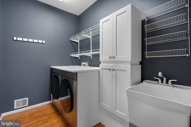 laundry room featuring visible vents, a sink, washer and dryer, light wood finished floors, and baseboards
