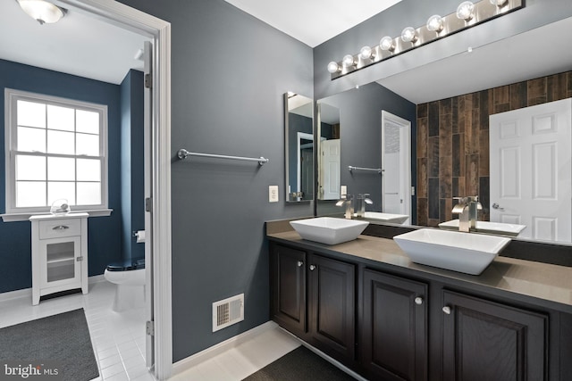 bathroom with visible vents, toilet, a sink, double vanity, and baseboards
