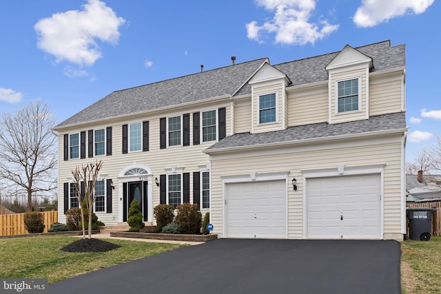 colonial home featuring a front lawn, an attached garage, aphalt driveway, fence, and a shingled roof