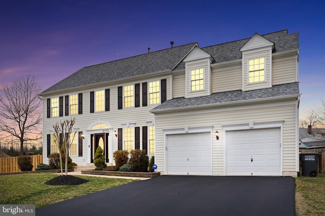 colonial inspired home featuring aphalt driveway, a garage, a front yard, fence, and a shingled roof
