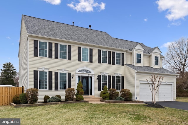 colonial-style house with a front yard, driveway, fence, and an attached garage